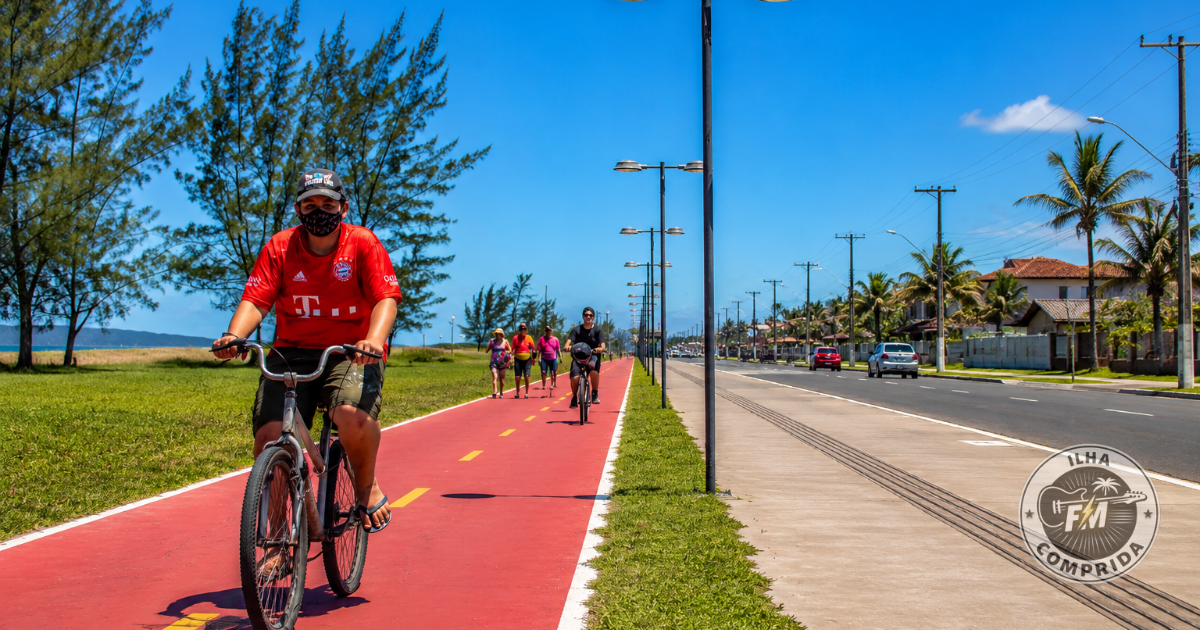Ciclovia de Ilha Comprida com ciclistas e pedestres em uma área próxima à praia e à avenida principal da cidade.